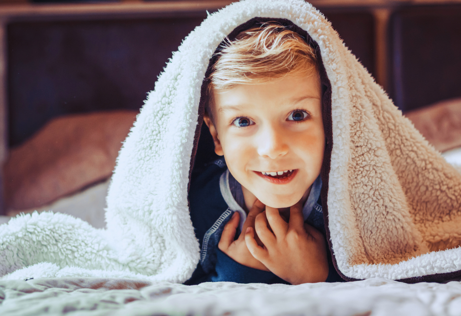 Kid smiling with blanket over head. 